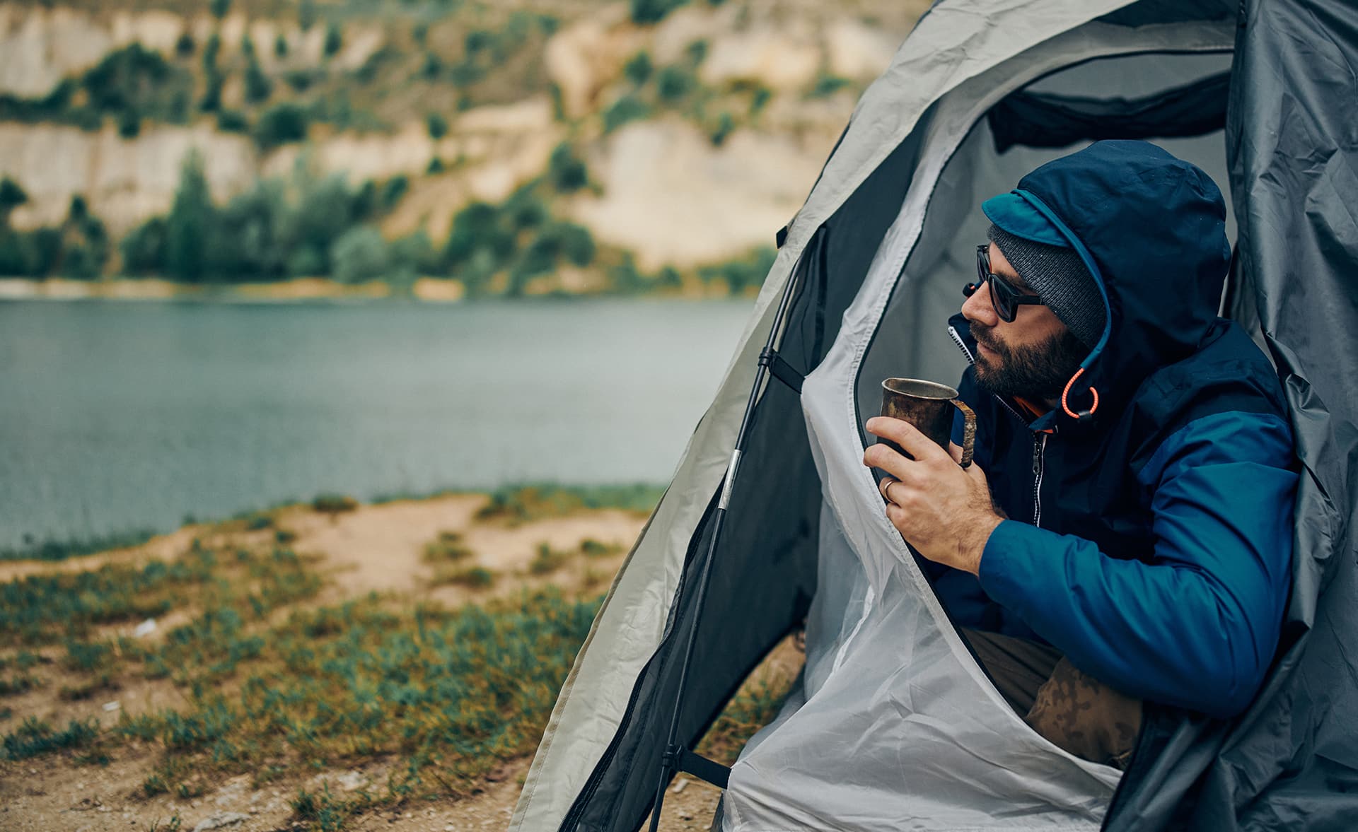 Man with a beard camping in a tent with outdoor scene in background